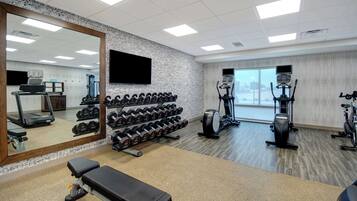 A gym with a treadmill, dumbbells, a bench, and exercise machines.