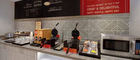 A breakfast bar with waffle makers, a microwave, and waffle boxes.