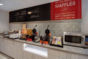 A breakfast bar with waffle makers, a microwave, and waffle boxes.