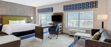 A hotel room with a bed, desk, chair, and a sofa.