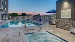 A swimming pool with a hot tub, lounge chairs, and umbrellas.