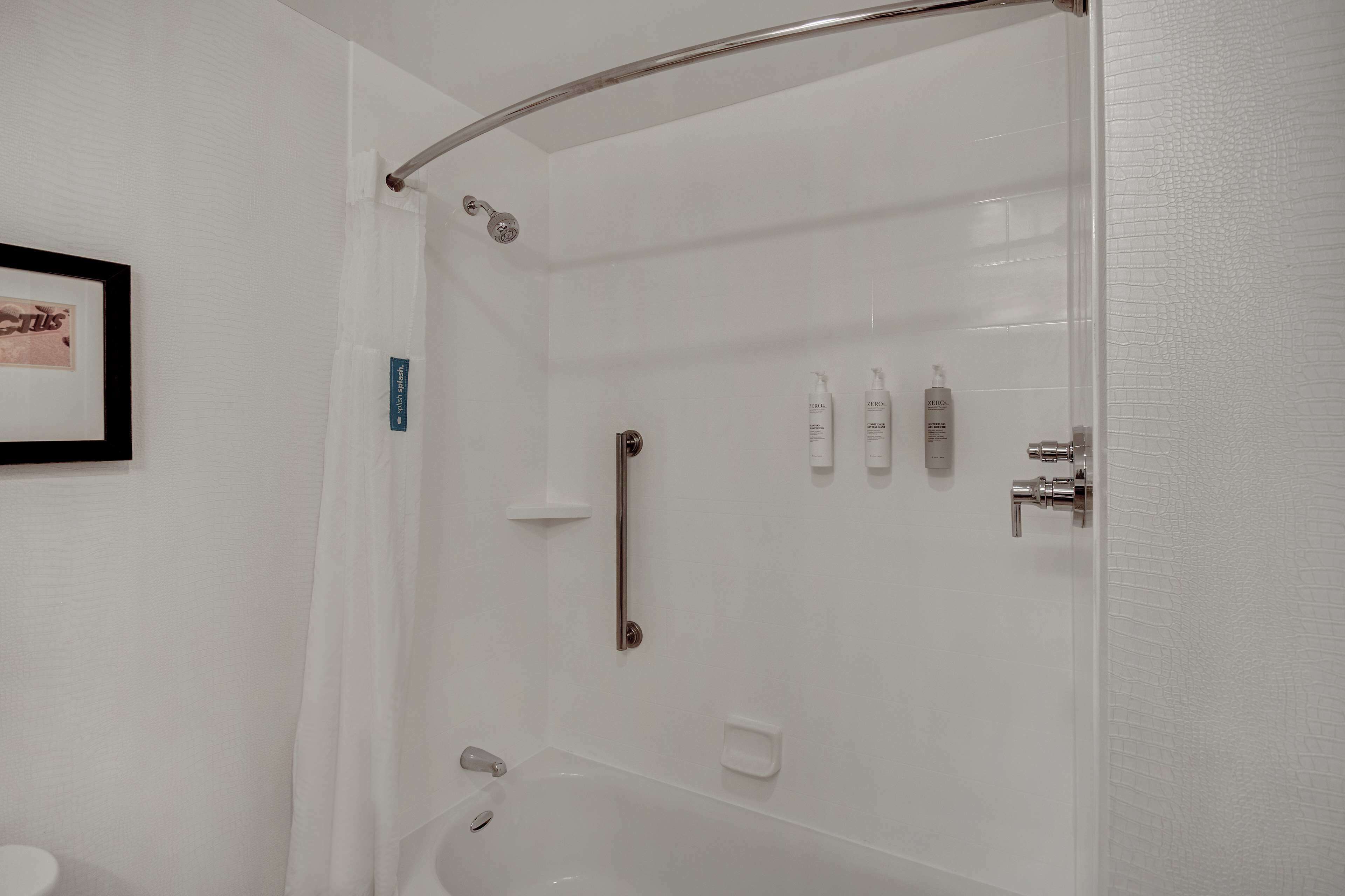 Un baño moderno con ducha de vidrio, lavamanos blanco y un cuadro enmarcado en la pared.