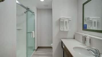 Un bany modern amb una dutxa de vidre, un lavabo blanc amb mirall i tovalloles netes i ben plegades a l'estant.