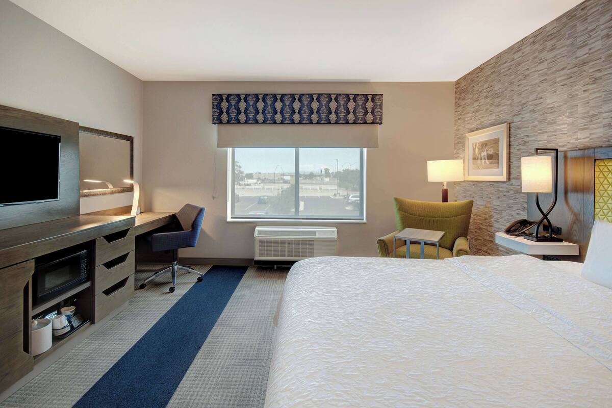A hotel room with a bed, desk, chair, TV, and a window with a view.
