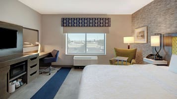 A hotel room with a bed, desk, chair, TV, and a window with a view.