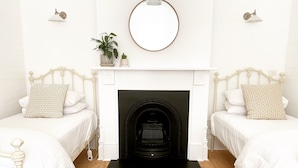 A bedroom with two beds, a fireplace, a mirror, and wall-mounted lamps. - Castlebar - Superior Boutique Accomodation - Steps to Pakington Street (Geelong West)