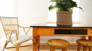 A wooden dining table with a woven plant pot, a wicker chair, and two wooden stools. - Castlebar - Superior Boutique Accomodation - Steps to Pakington Street (Geelong West)