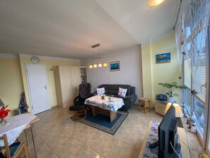 A living room with a sofa, a dining table with chairs, a TV, and a window with a view. - Steinhagen A. Timmendorf Beach - Vacation Home in Timmendorf Beach (Insel Poel)