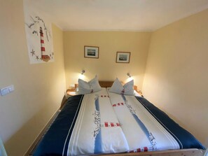 A neatly made bed with a striped bedspread, two bedside tables with lamps, and two framed pictures on the wall. - Steinhagen A. Timmendorf Beach - Vacation Home in Timmendorf Beach (Insel Poel)