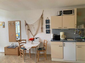 A compact kitchen with a wooden table, chairs, a refrigerator, a microwave, and a coffee maker. - Steinhagen A. Timmendorf Beach - Vacation Home in Timmendorf Beach (Insel Poel)