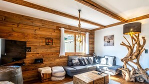 Ein gemütliches Wohnzimmer mit Holzvertäfelung, einem Ecksofa, einem Couchtisch und einem Fernseher.