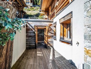 A wooden deck leading to a building with a stone wall and a window.