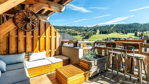 Eine Holzterrasse mit einer Couch, einem Holztisch und einem Barhocker.