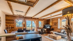 Ein rustikales Cabin-Interieur mit Essbereich, Sitzgelegenheiten, einem Fernseher und einem großen Fenster mit Blick auf die Berge.