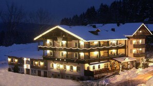 Ein großes, mehrgeschossiges Gebäude mit schneebedecktem Dach, umgeben von einer verschneiten Landschaft in der Nacht.