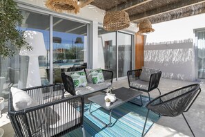 Une terrasse extérieure avec des meubles en osier, une porte vitrée donnant accès à une piscine et une vue sur les environs.