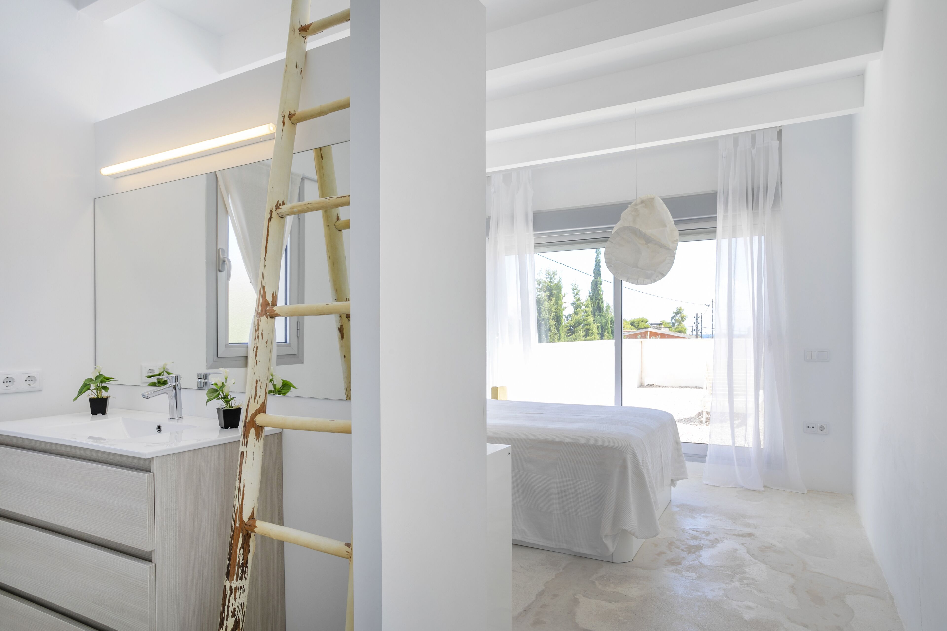 Een moderne slaapkamer met een groot raam, een bed en een badkamer met een wastafel en planten.