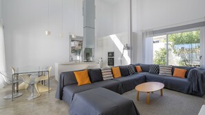 A modern living room with a sectional sofa, a glass dining table, and a kitchen in the background.