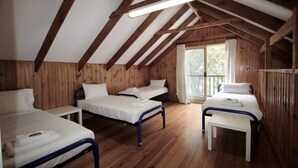 Une chambre de dortoir avec trois lits superposés, des murs en bois et un plafond en pente avec des poutres apparentes.