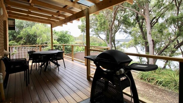 Une terrasse en bois avec un barbecue, des sièges d’extérieur et une vue sur les arbres et l’eau.
