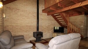 Un salon avec deux canapés en cuir, un téléviseur et un poêle à bois.