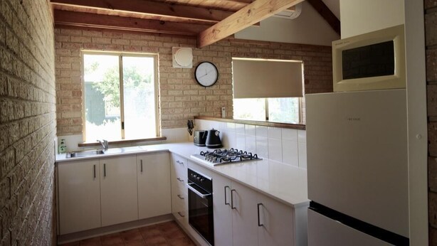 Una cocina con gabinetes blancos, una estufa a gas, un refrigerador y un reloj en la pared.