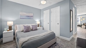 A bedroom with a bed, nightstands, a ceiling fan, and a door.