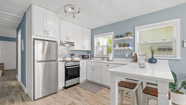 A modern kitchen with white cabinets, stainless steel appliances, and a white dining table with bar stools.