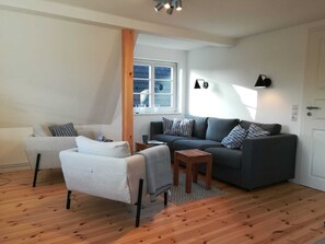 Una sala de estar moderna con un sofá gris, un sillón blanco y una mesa de centro de madera.