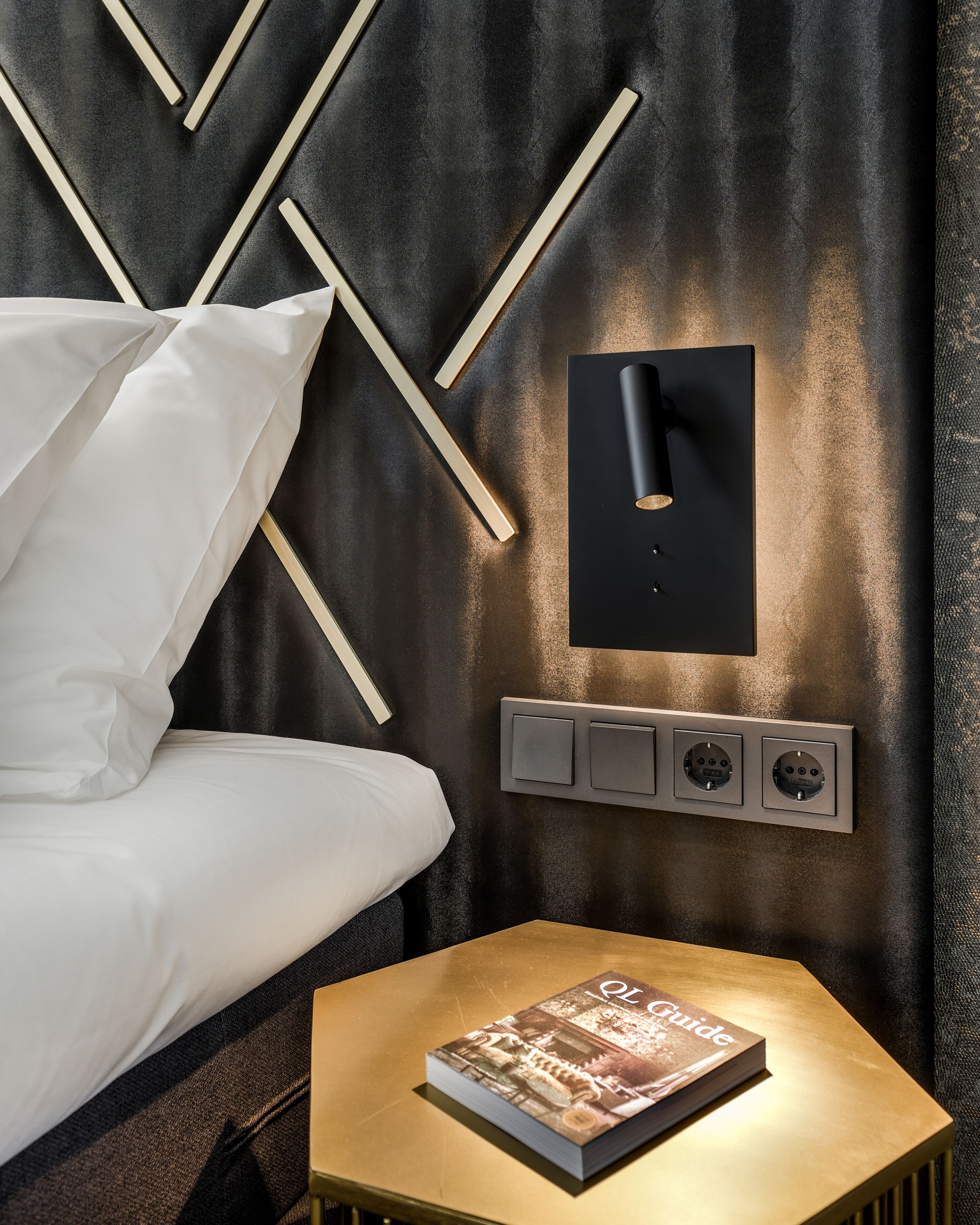 A modern bedroom with a bed, bedside table, and a wall-mounted light fixture.