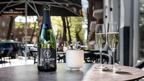 Uma garrafa de vinho Le Marin e duas taças de champanhe sobre uma mesa ao ar livre.