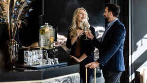 Um homem e uma mulher estão num bar, perto de um grande recipiente de vidro e uma planta decorativa.