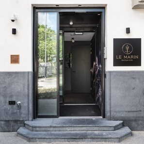 The entrance to Le Marin Boutique Hotel with a glass door, a signboard, and a plaque on the wall.
