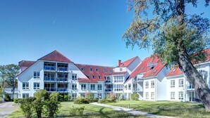 En stor, fleretagers bygning med rødt tegltag, omgivet af velholdte græsplæner og træer.