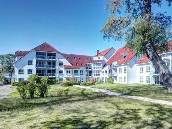 Een groot, meerlaags gebouw met een rode pannendak, omringd door goed onderhouden gazons en bomen.