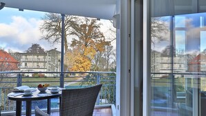 En balkon med et bord, stole og udsigt til bygninger og træer.
