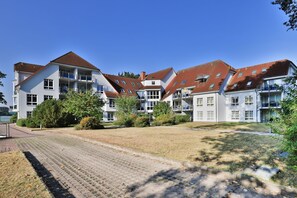 Een woongebouw met meerdere balkons, een bestraat binnenterrein en omliggend groen.