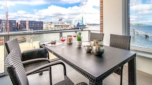 A balcony with wicker furniture, a table with decorative items, and a view of a marina and buildings. - Hafenspitze App. 16 Pier 2.16 (Wismar)