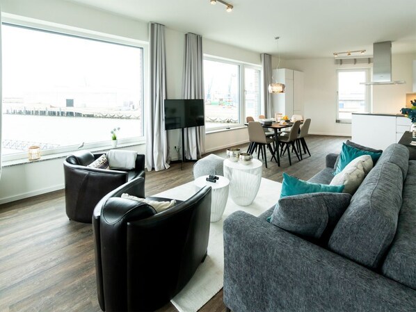 A modern living room with a grey sofa, black leather armchair, and a dining area with a table and chairs.