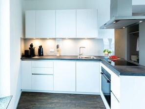 A modern kitchen with white cabinets, a stainless steel sink, and a built-in oven. - Hafenspitze App. 16 Pier 2.16 (Wismar)