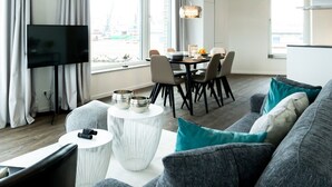 A modern living room with a sofa, a dining table, and a TV. - Hafenspitze App. 16 Pier 2.16 (Wismar)