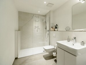 A modern bathroom with a glass-enclosed shower, a toilet, a sink, and a mirror. - Hafenspitze App. 16 Pier 2.16 (Wismar)
