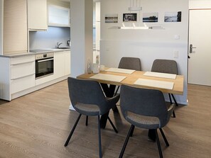 Une cuisine moderne avec des meubles blancs, un four encastré et un coin repas comprenant une table en bois et quatre chaises.
