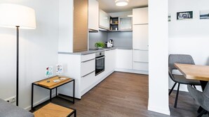 Una cucina compatta con mobili bianchi, un piano di lavoro in legno, un piccolo tavolo con lampada e un'area pranzo con una sedia.