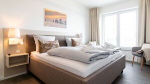 Camera d'albergo moderna con un letto grande, comodini, una poltrona e un'ampia finestra con tende.