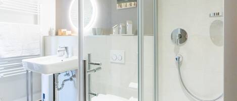 A modern bathroom with a glass shower enclosure, a white sink, and a toilet.