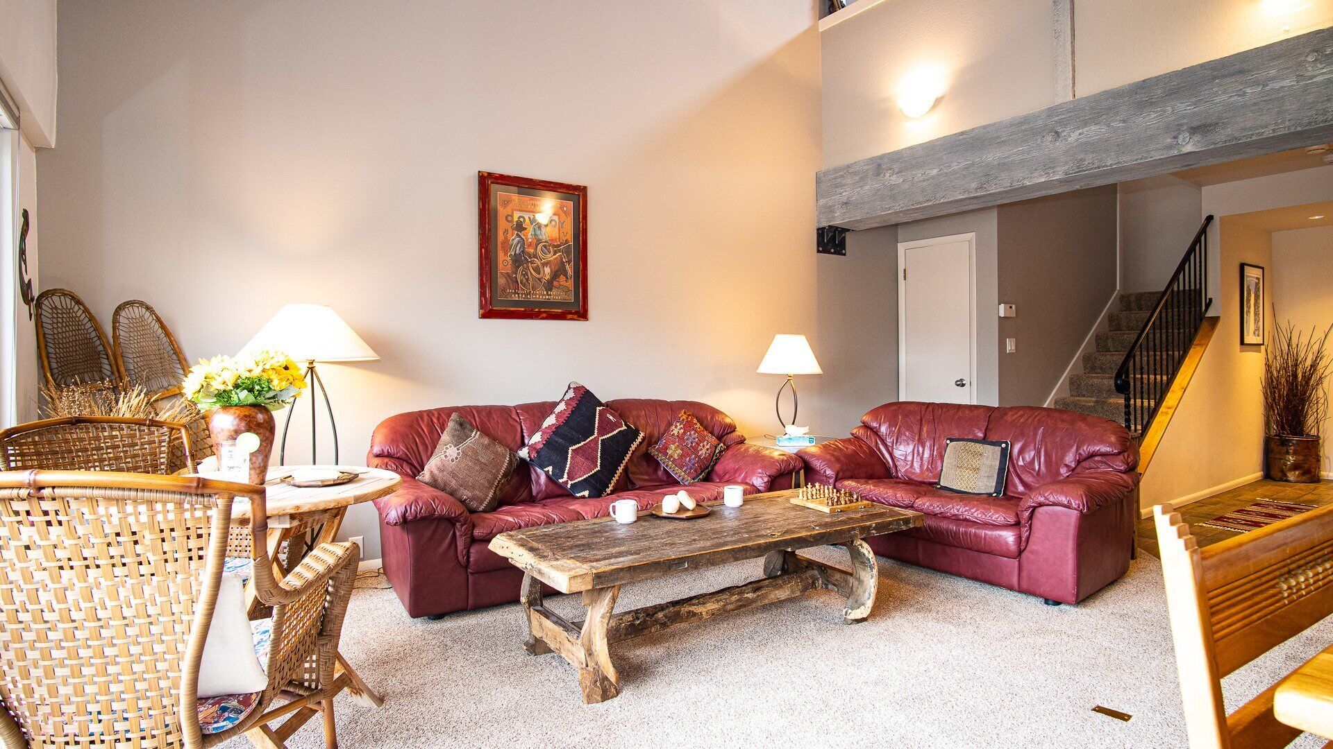 Ein gemütliches Wohnzimmer mit einem roten Ledersofa, einem Holztisch, Korbstühlen und einem Bild an der Wand.