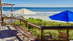 Eine Holzterrasse mit Sitzgelegenheiten und Sonnenschirmen mit Blick auf einen Strand.