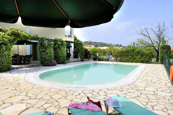 A swimming pool with stone tiles, a covered seating area, and a view of the surrounding landscape.