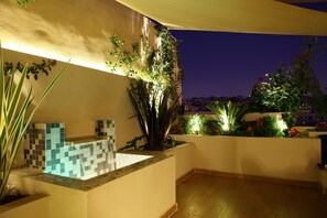 An outdoor terrace with a tiled water feature, potted plants, and a view of the cityscape at dusk. - Eco Two bed Apartment With Roof Garden in Amman (Amman)